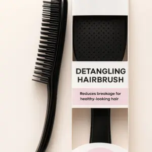 Black detangling hairbrush with flexible two-length bristles lying beside its white and pink retail box