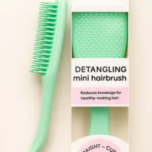 Mint green mini detangling hairbrush next to its white and pink box marked straight to curly